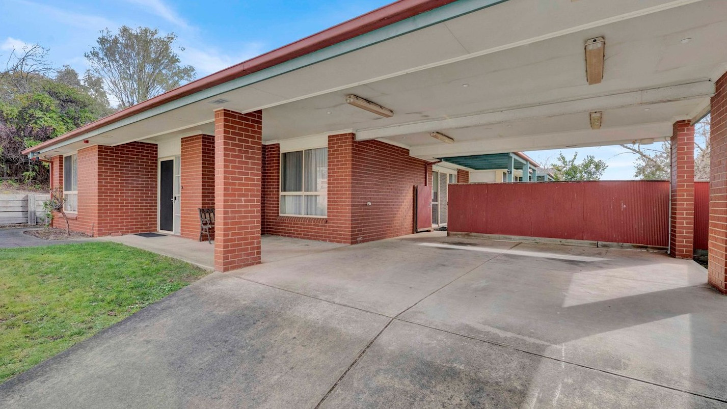 Brick home exterior with large covered carport or outdoor space, concrete driveway, and small lawn.