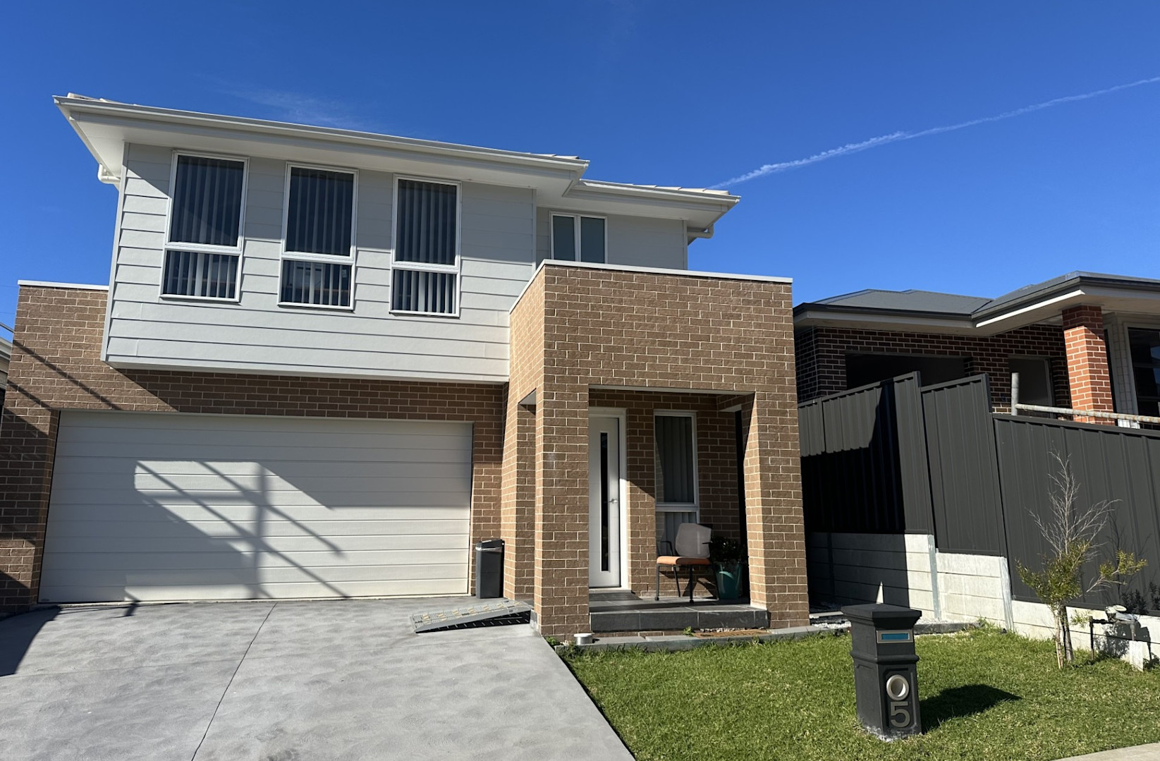 Modern double-storey home with a mix of light cladding and brick exterior, double garage, and small front lawn with house number 5 on a black letterbox.