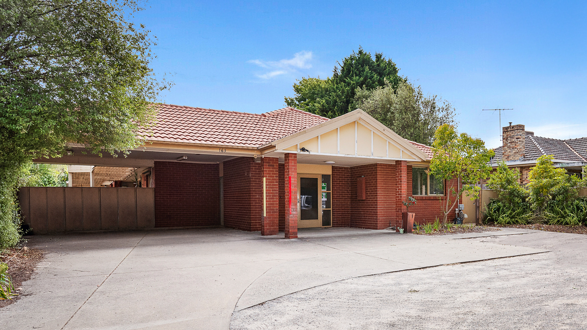 Front of the house with a brick exterior. A concrete driveway leads to a carport with a path to the front door.