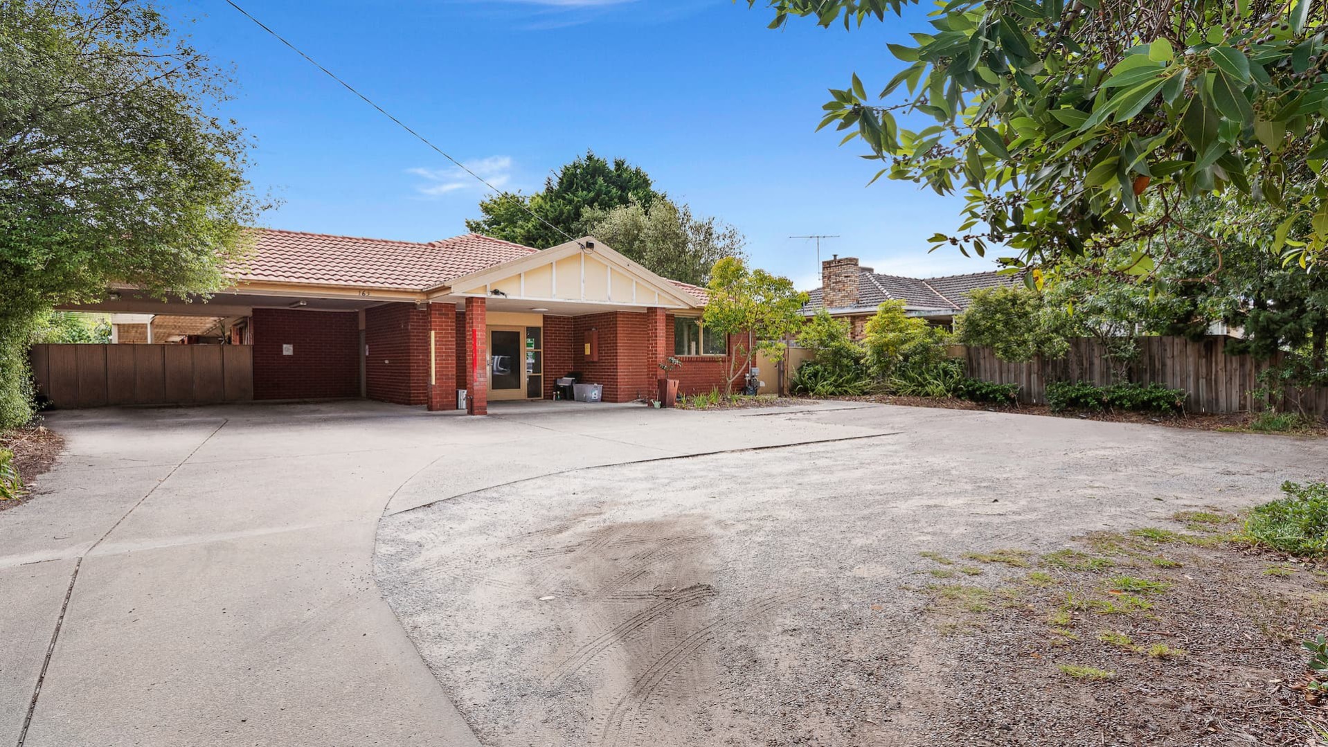 Front of the house with a brick exterior. A concrete driveway leads to a carport with a path to the front door. 