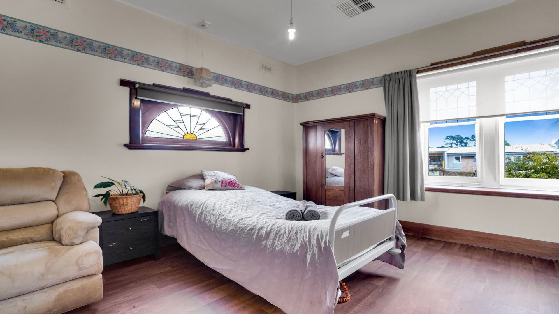 beautifully presented spacious bedroom with stained glass window, wooden free standing wardrobe, bed, side table and armchair.