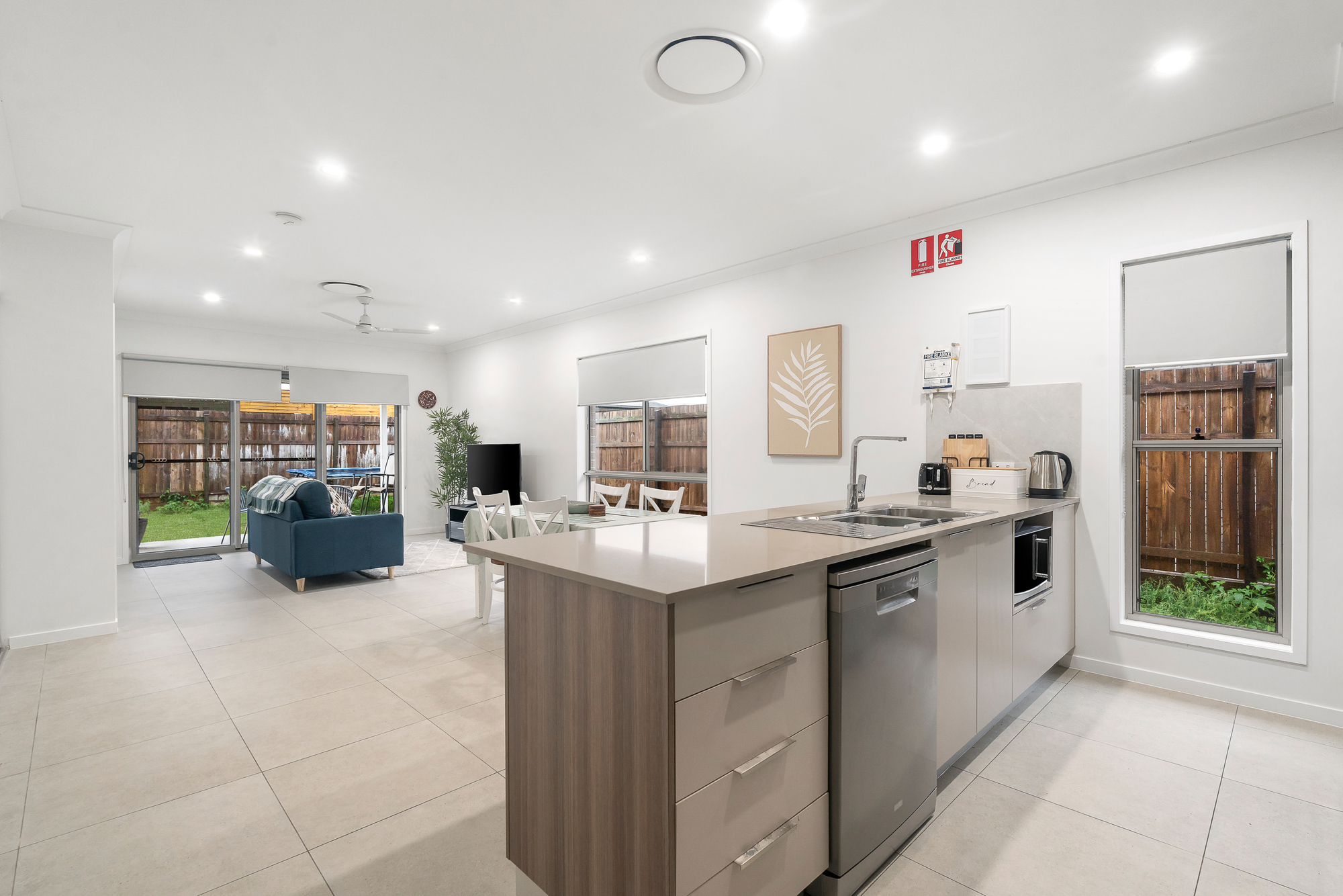 Open-plan kitchen with island bench, stainless steel appliances, and adjoining living area with blue sofa and dining table.