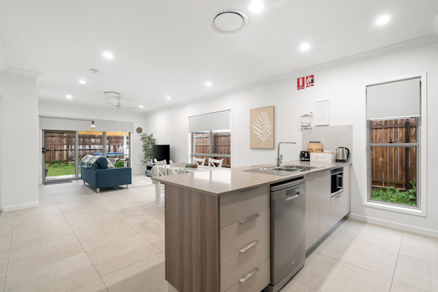Open-plan kitchen with island bench, stainless steel appliances, and adjoining living area with blue sofa and dining table.