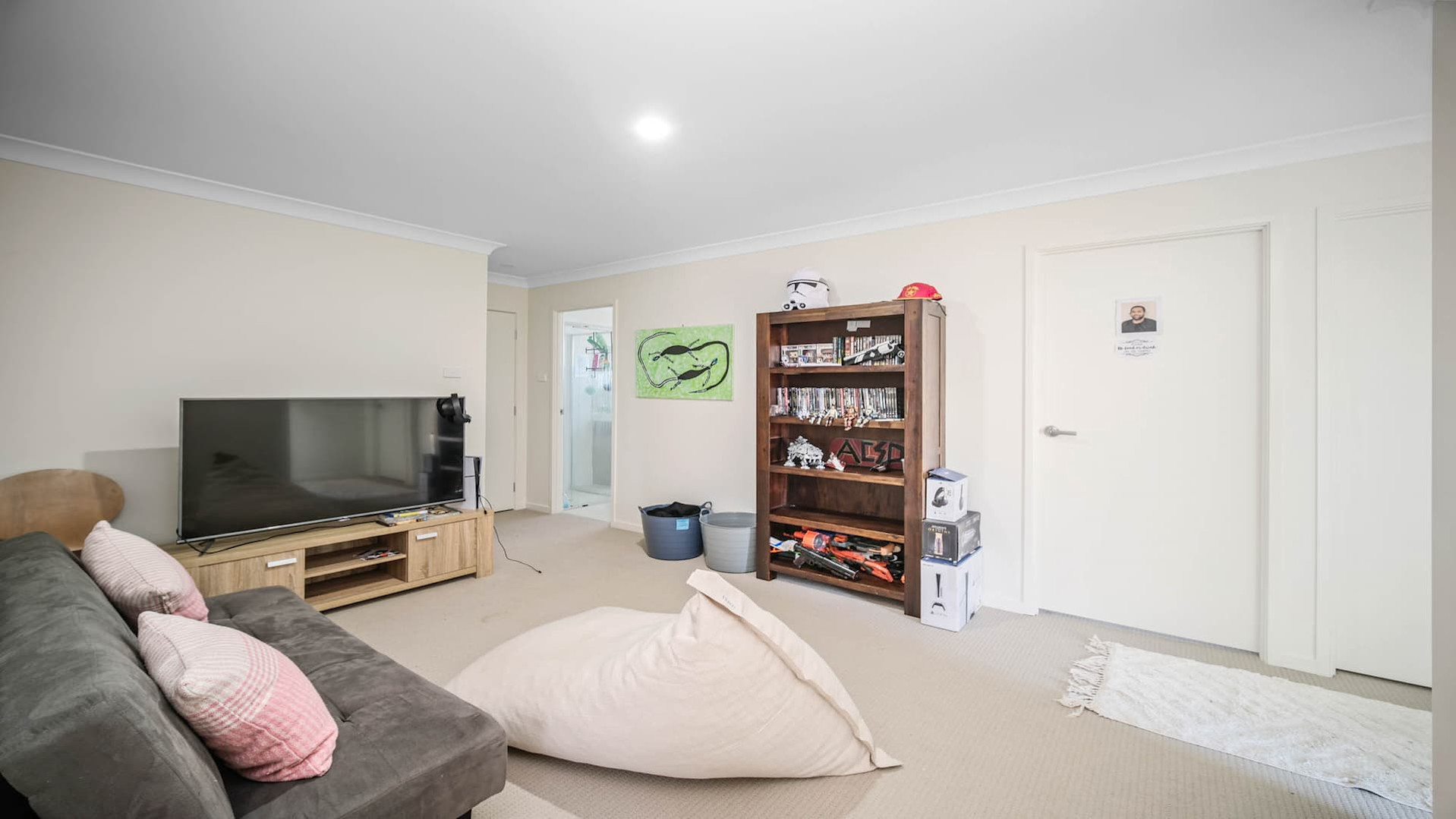Carpeted floor, bookshelf, grey couch with pink cushions.