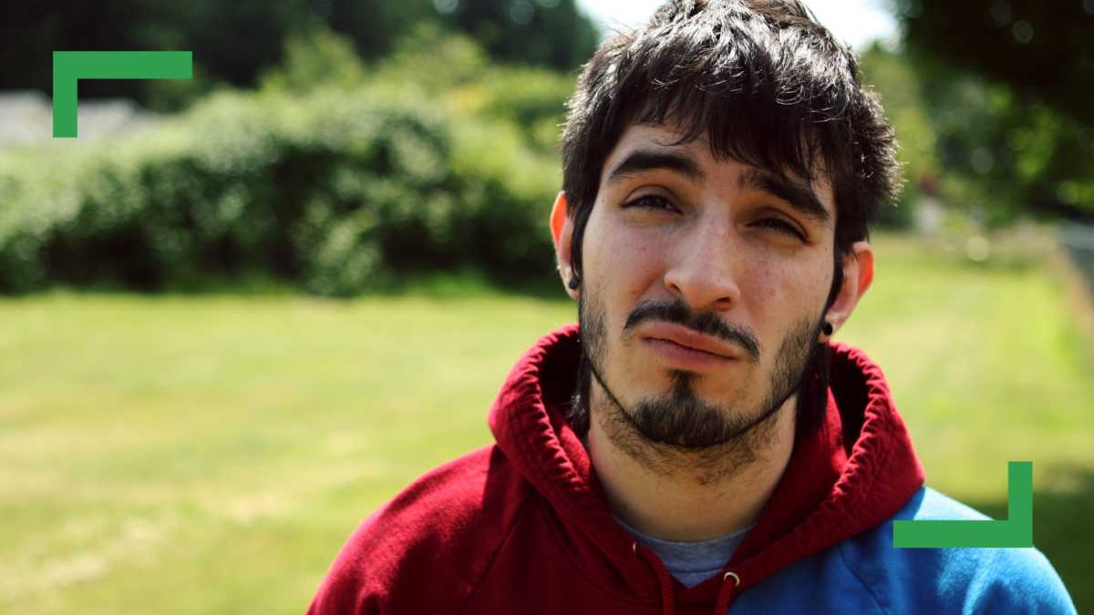 Close-up of a man with dark hair, a beard and a hoodie standing outside.