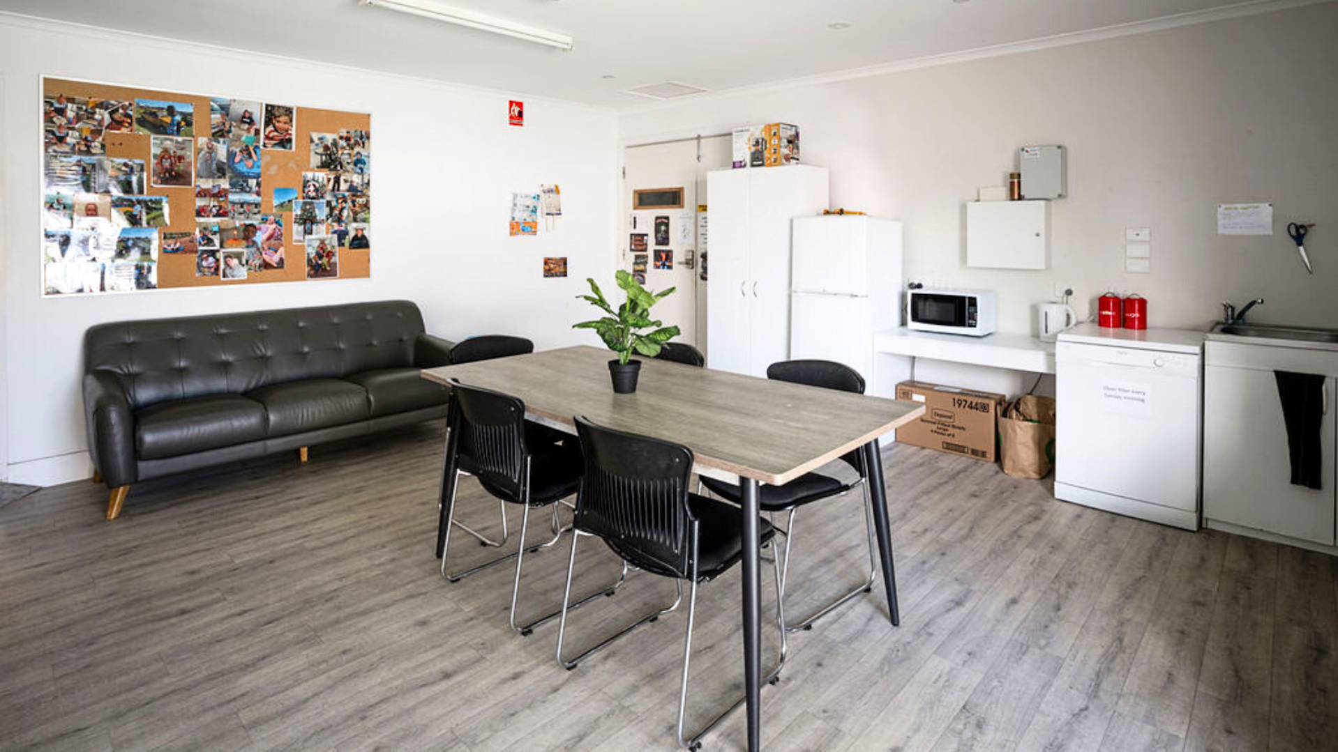 Dining area with a dining table and a black couch. Against the wall are fridges and cupboards.