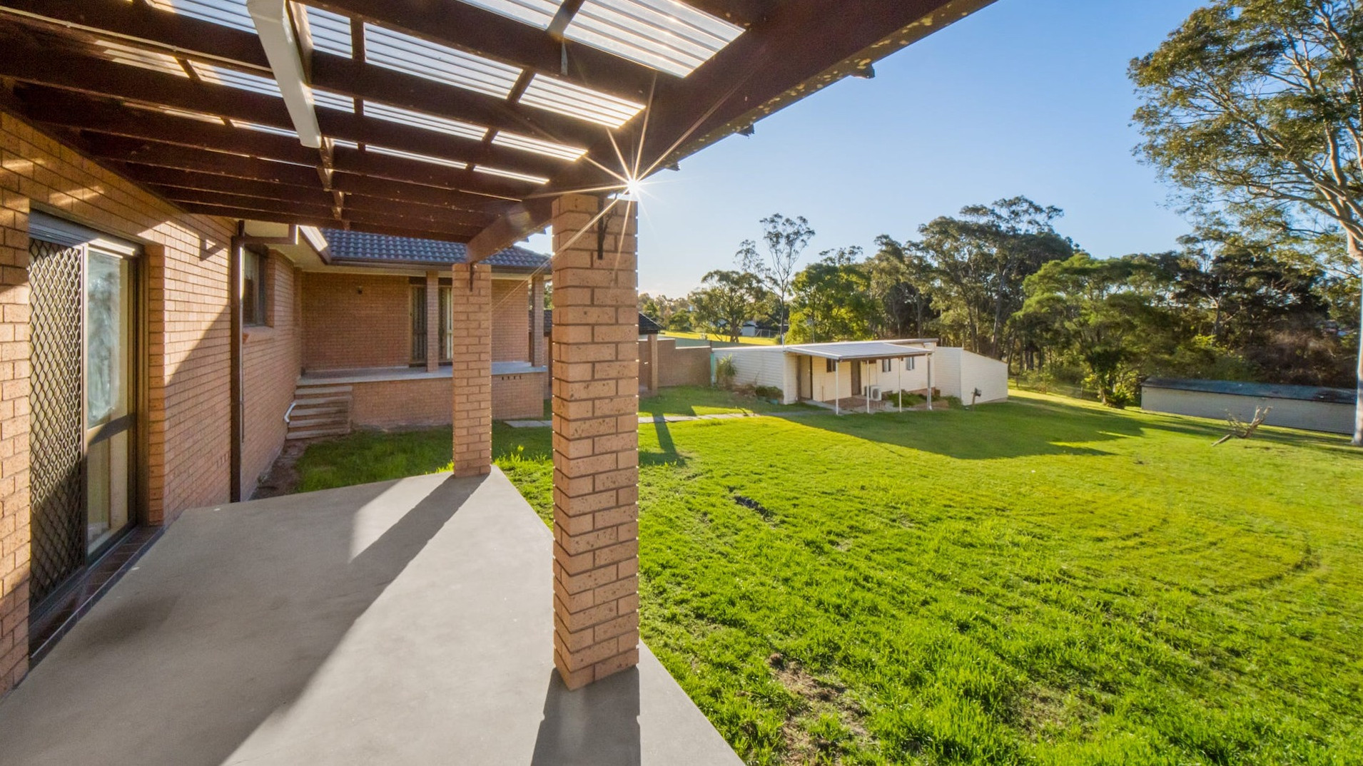 Covered patio with brick posts overlooking a large green backyard and shed.