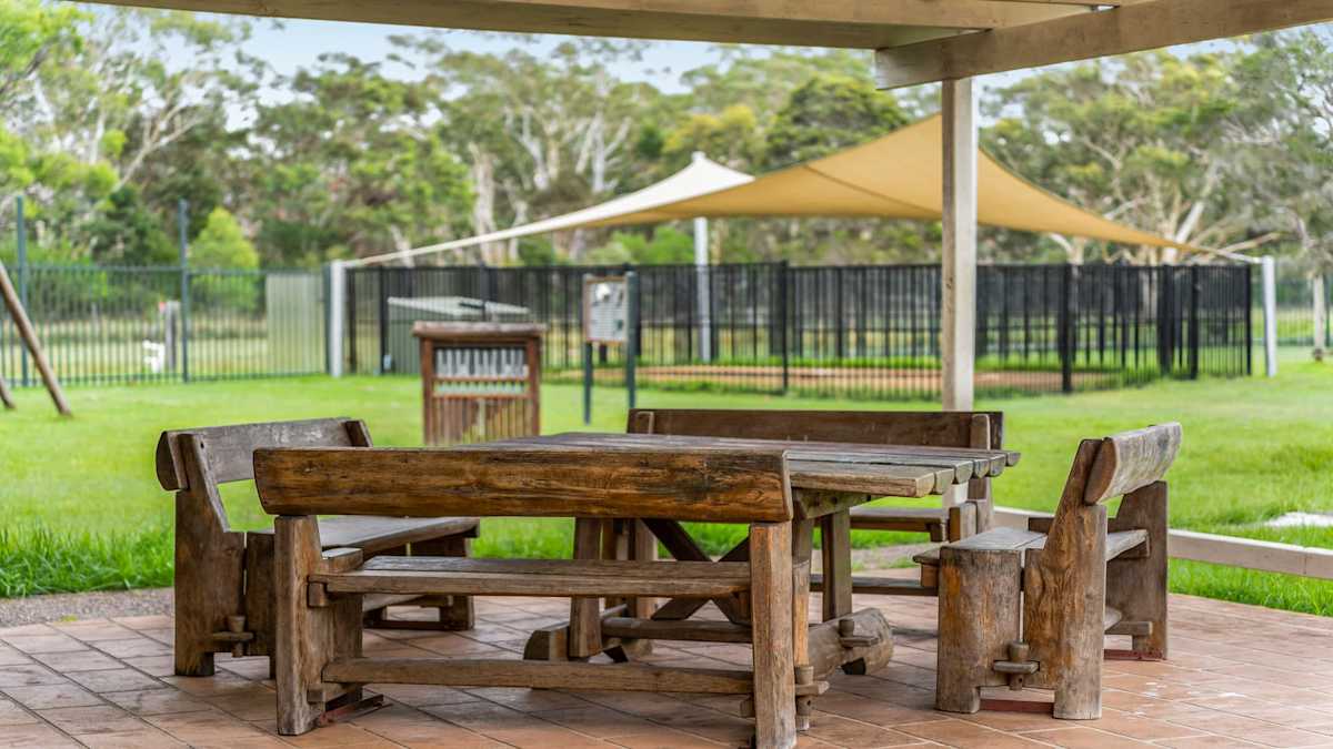 Outdoor undercover entertainment area with wooden table and benches, overlooking the backyard and swimming pool.