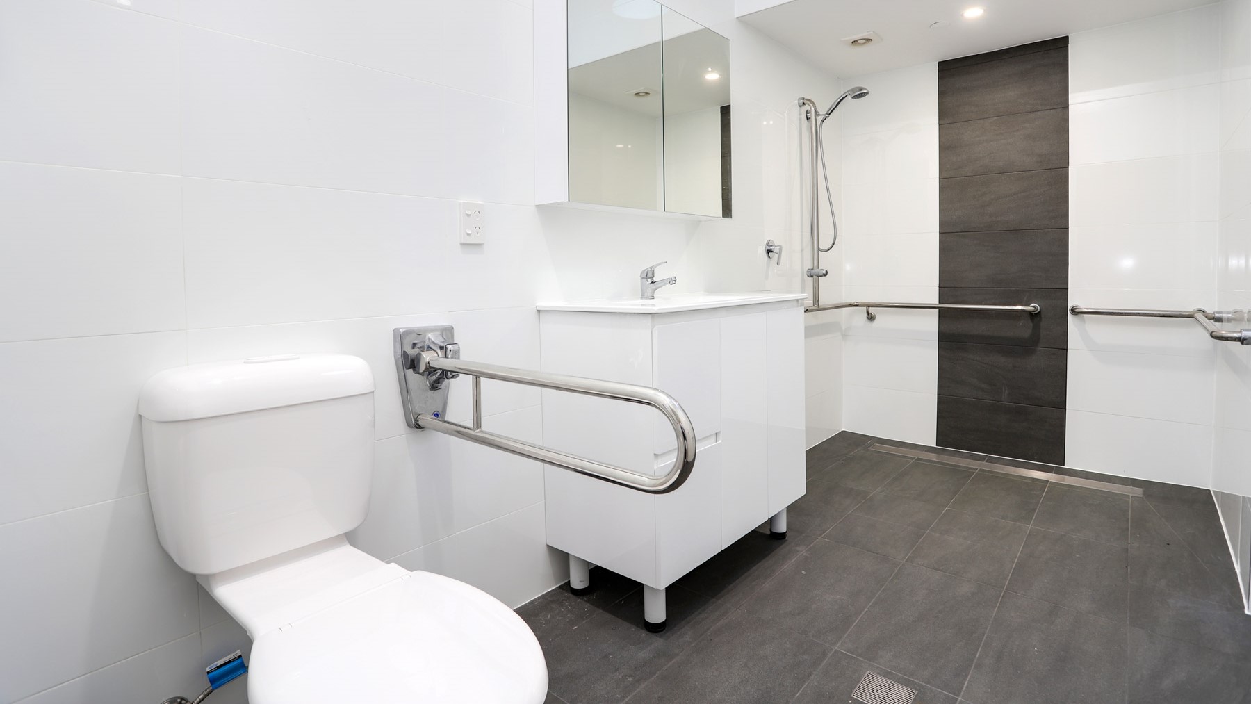 Open plan bathroom with grab rails, stepless shower, shower chair and toilet.