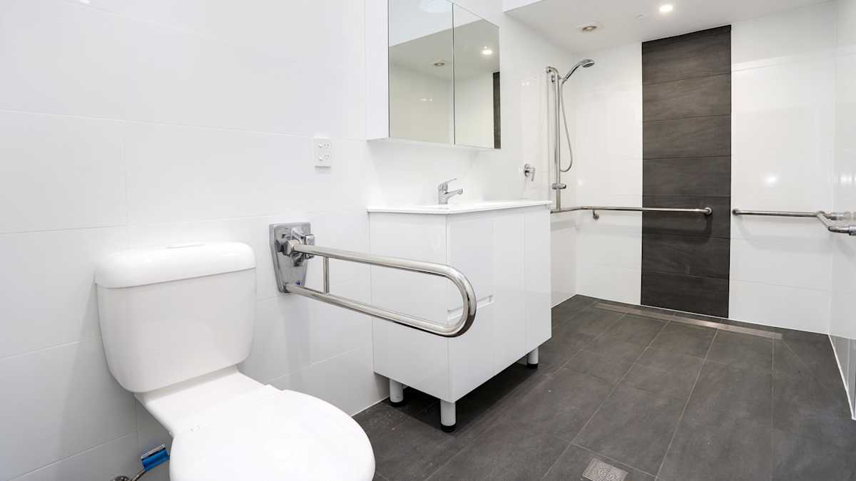 Open plan bathroom with grab rails, stepless shower, shower chair and toilet.