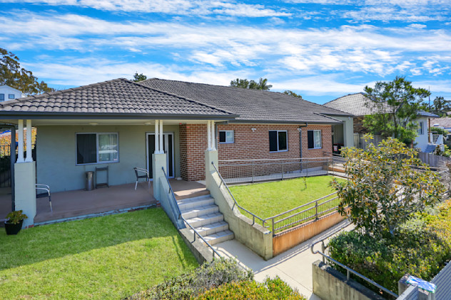 Front view of accessible brick home with tiled roof, veranda, steps, and ramp leading to entry.