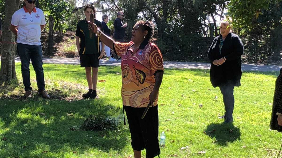Aunty Bridgette Chilli standing outdoors performing a smoking ceremony.