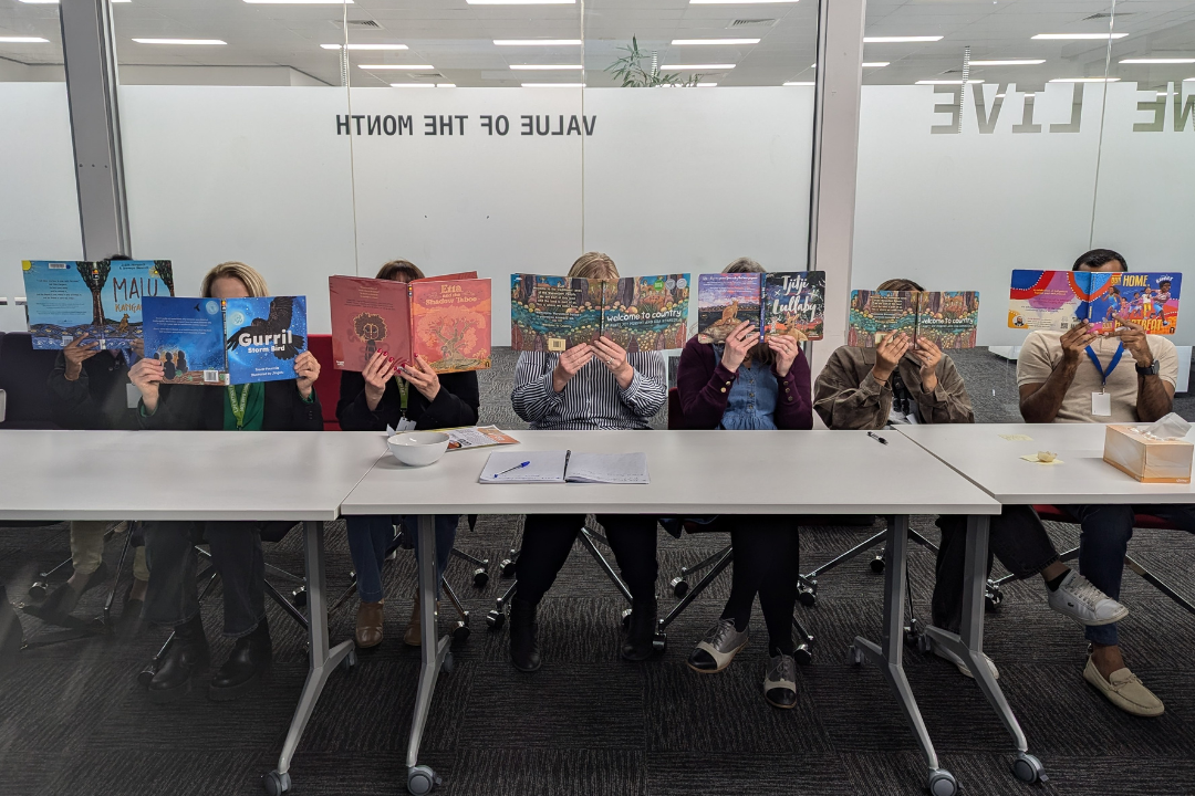 The Victorian Child, Youth, and Family team sitting at a table, holding books over their faces.