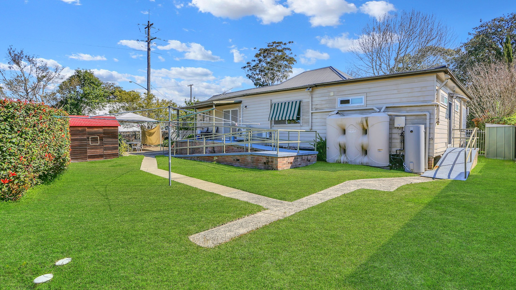 Spacious backyard with green lawn, clothesline, garden shed, and accessible ramps leading to house.