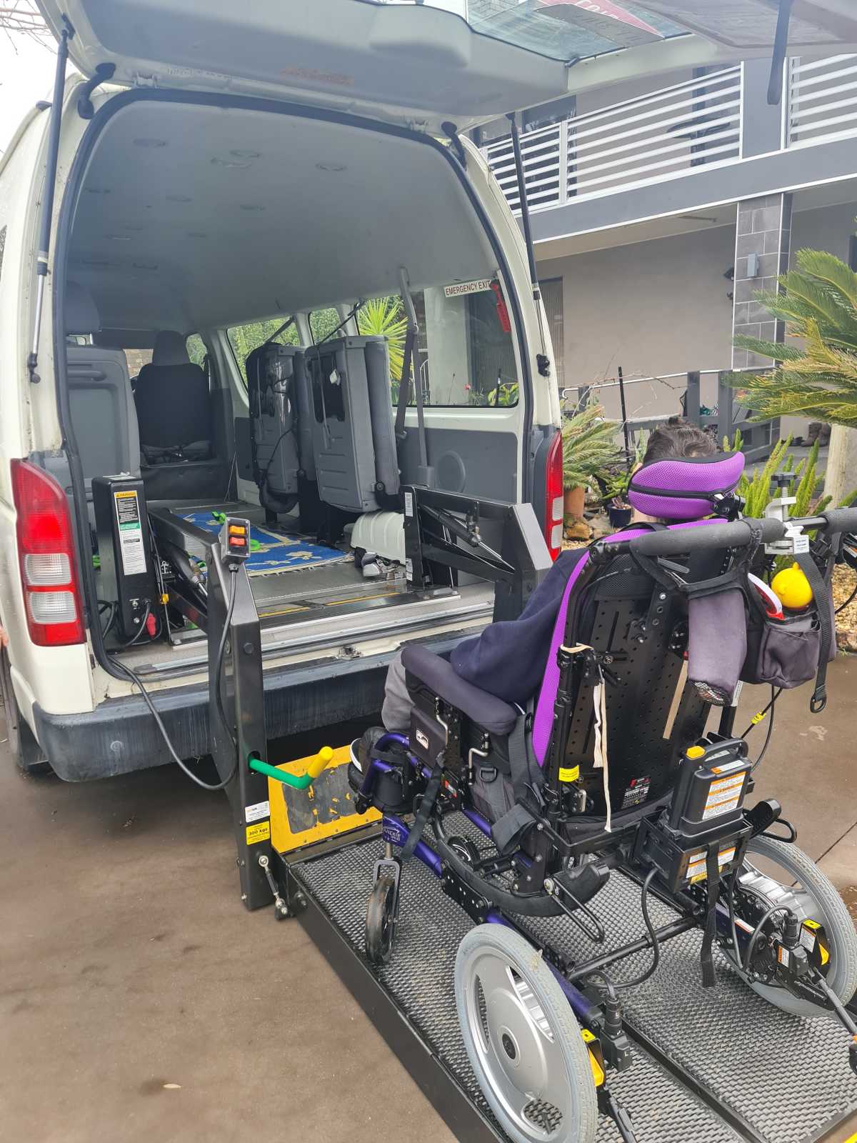 The back of a large white van with a wheelchair being lifted into the van.
