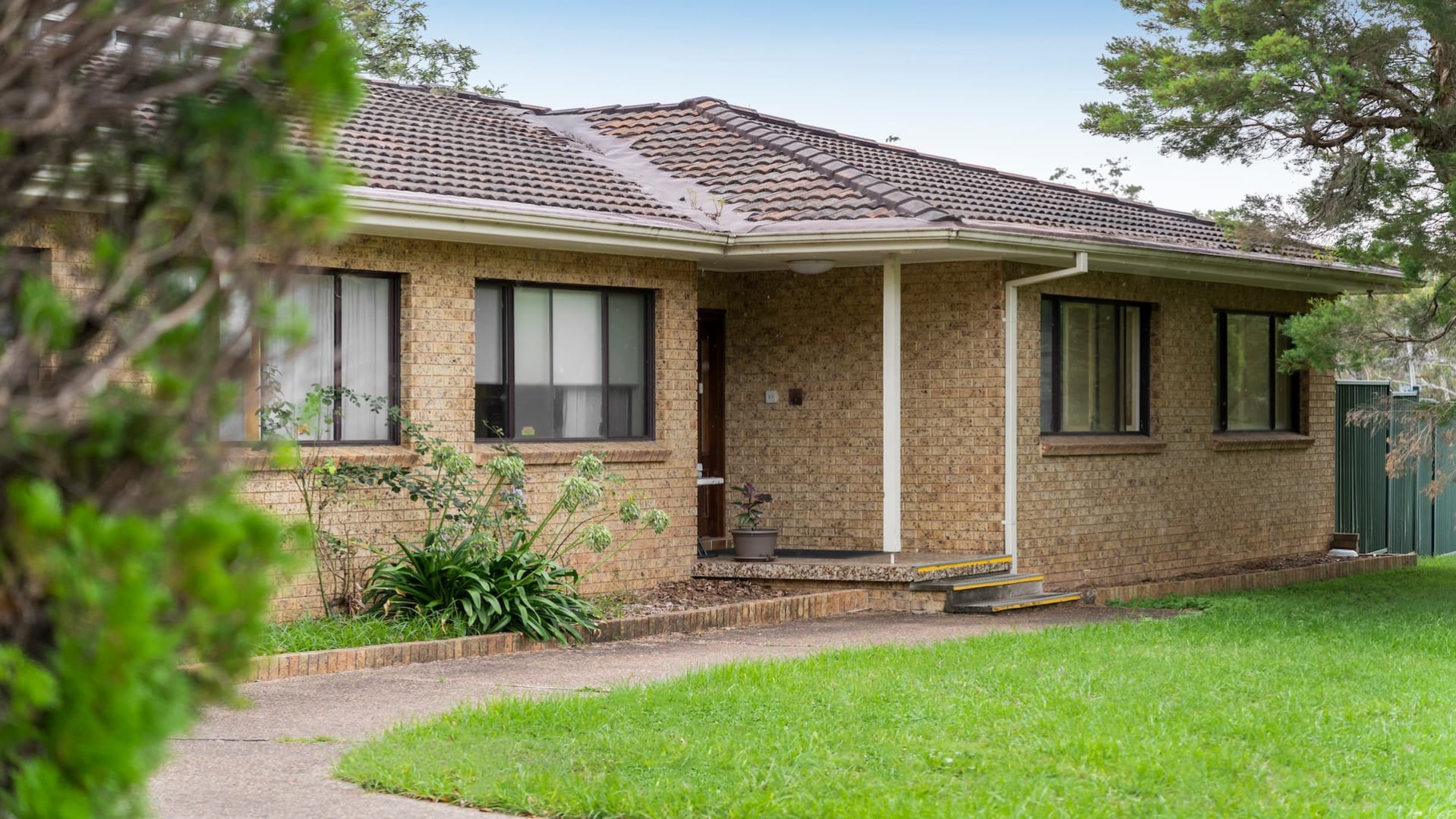 House with a brick facade, a concrete pathway leading to steps to access the front door and a grass area in the front yard.