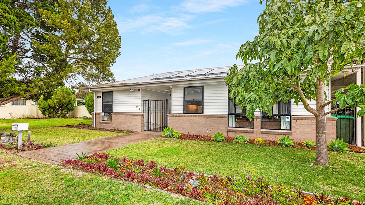 Single-story residential home with a well-maintained front garden, white and brick exterior, and solar panels on the roof.