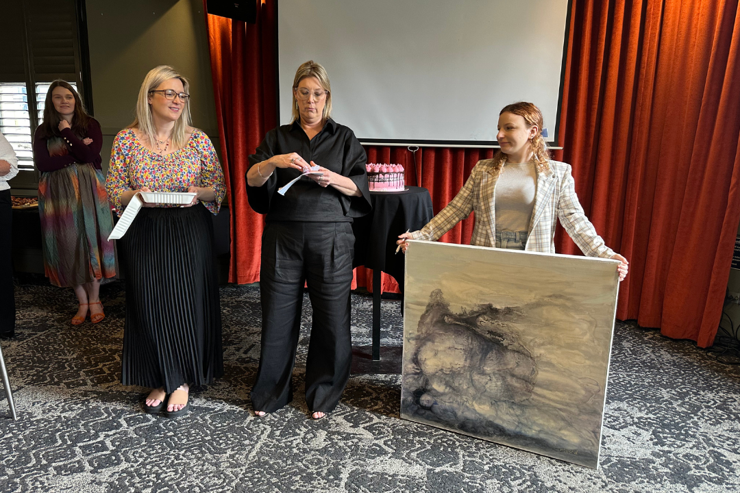 Rebecca, Kylie and Ruby holding up one of the raffle prizes, which is a painting.
