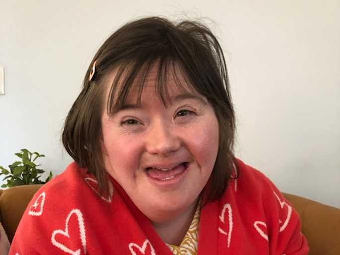 Livvy is wearing a red cardi with white hearts. She has short brown hair.