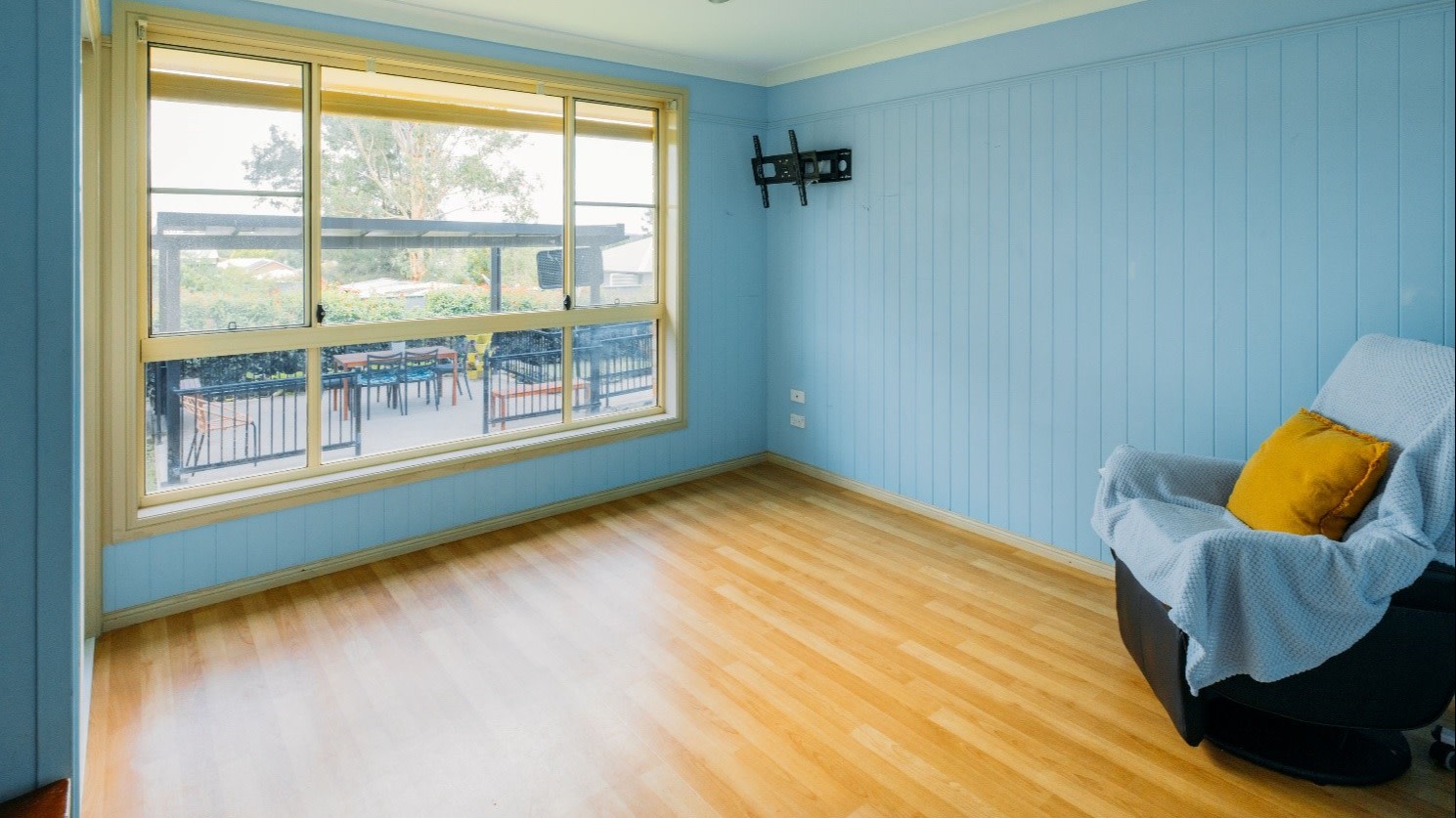 Well lit bedroom with light blue walls and wooden floor boards.