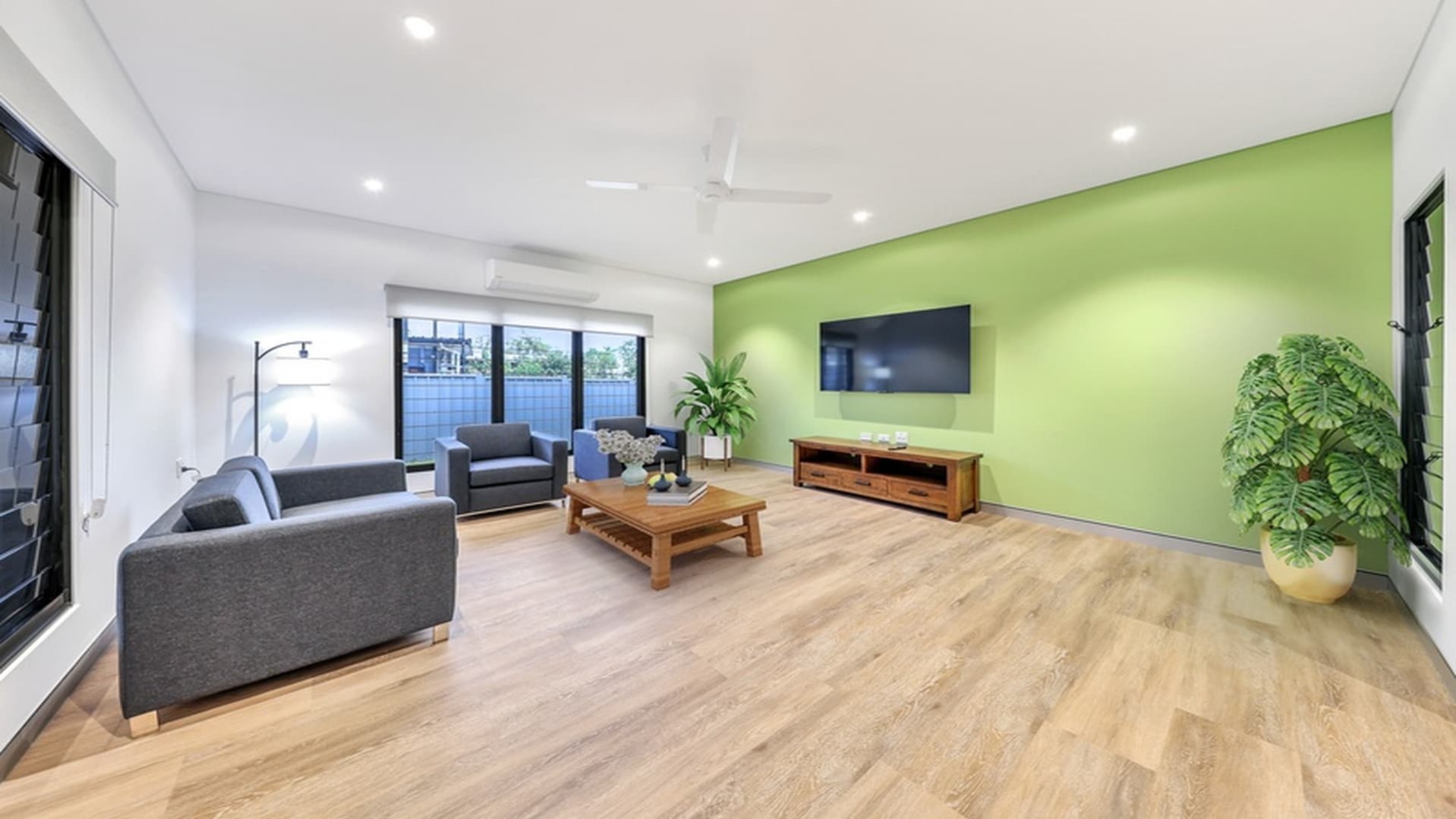 Spacious living room, open plan, hard flooring, green feature wall and large windows.