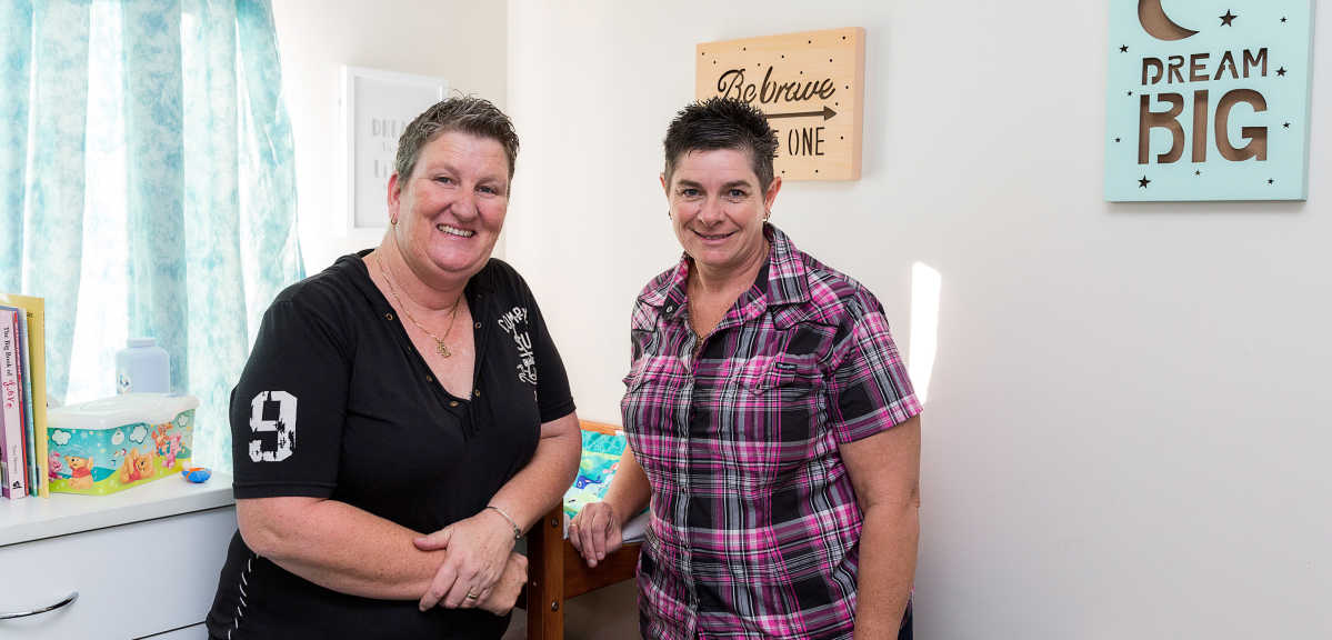Same-sex female foster carer couple in their forties in the nursery room smiling
