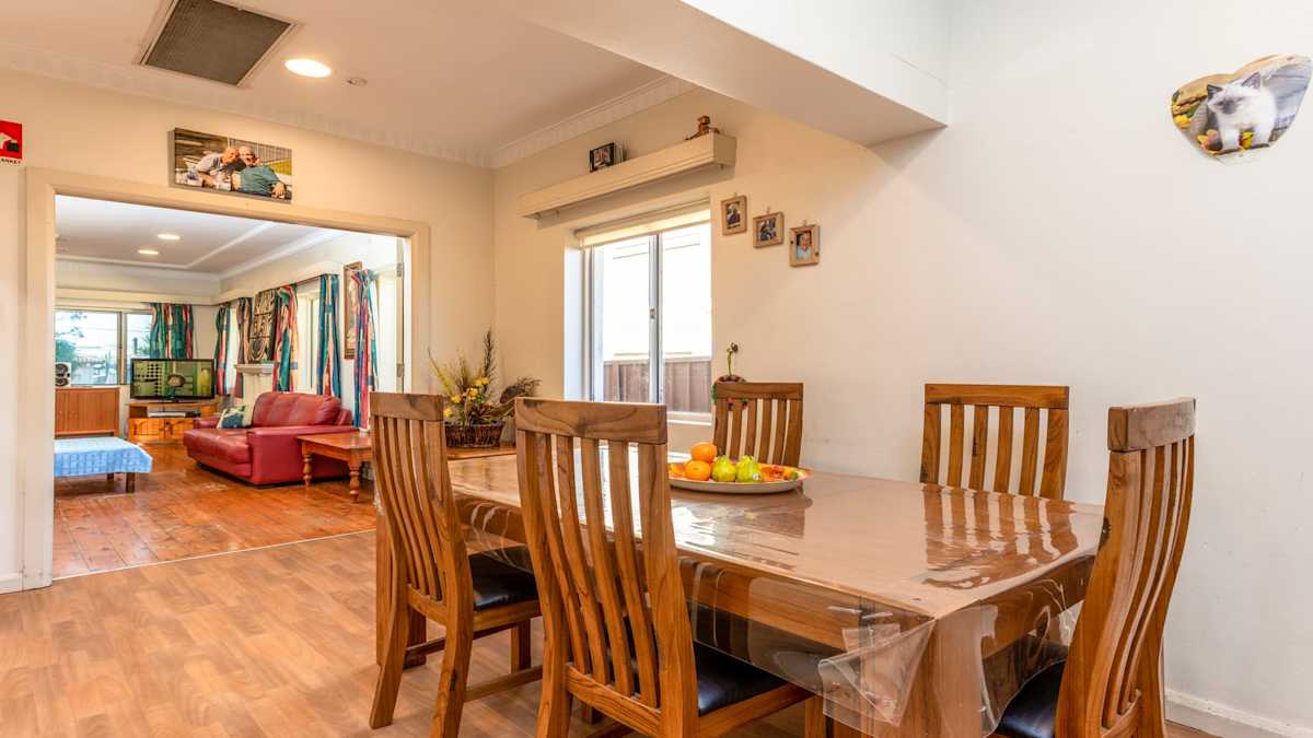 Combined dining and lounge room with wooden table set for five people opening out into the loungeroom with red couches and large windows.