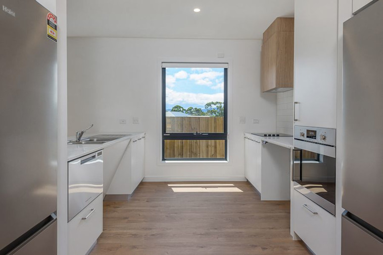 Spacious accessible kitchen with wide entry, timber floors, large window, white cabinets, built-in oven, cooktop, and stainless steel appliances.