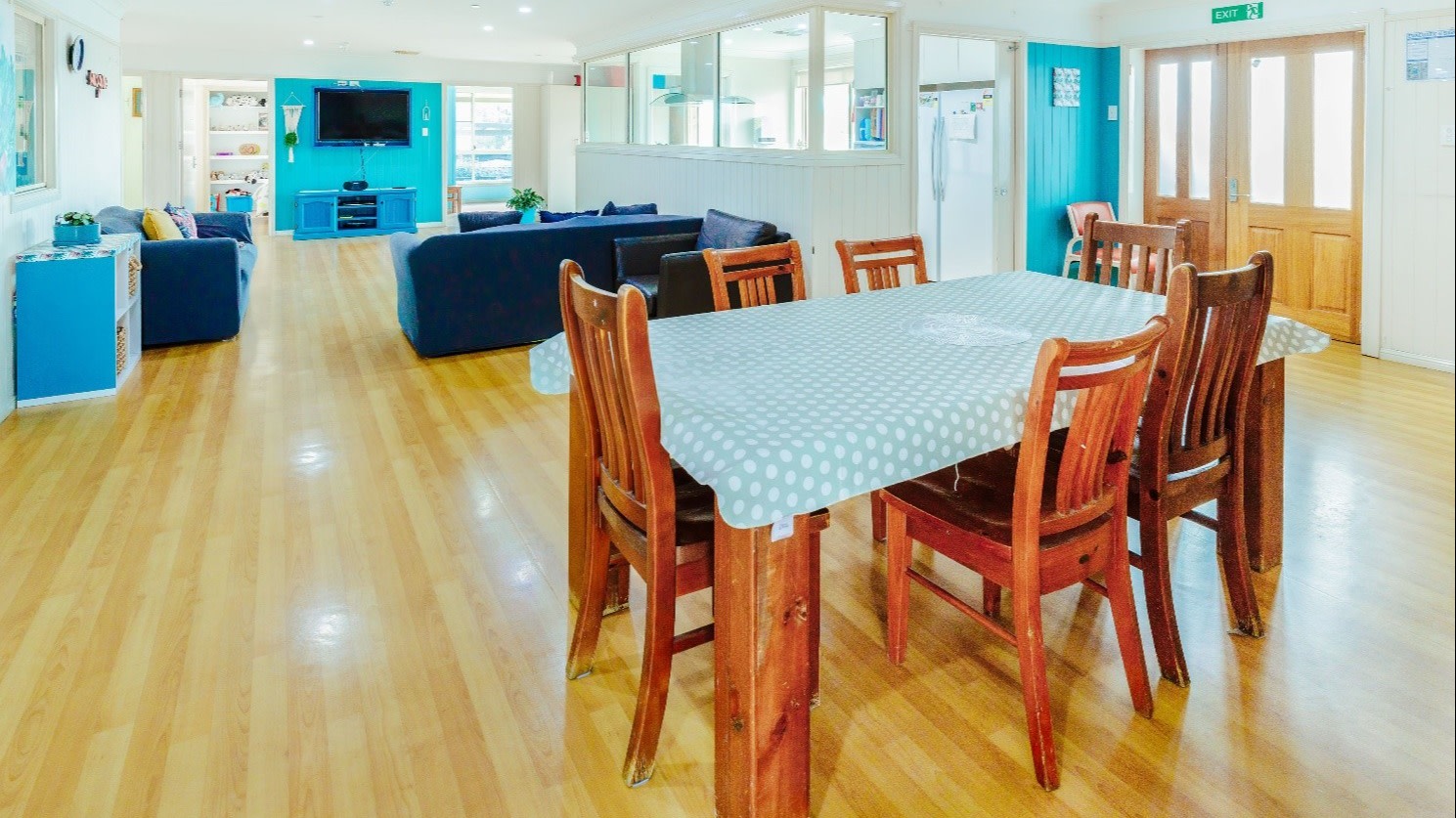 Kitchen and living room. Wooden floors and table. Blue walls and lounges. 