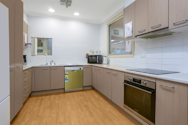 Modern kitchen with light wood cabinets, dishwasher, oven, microwave, and white tiled splashback.
