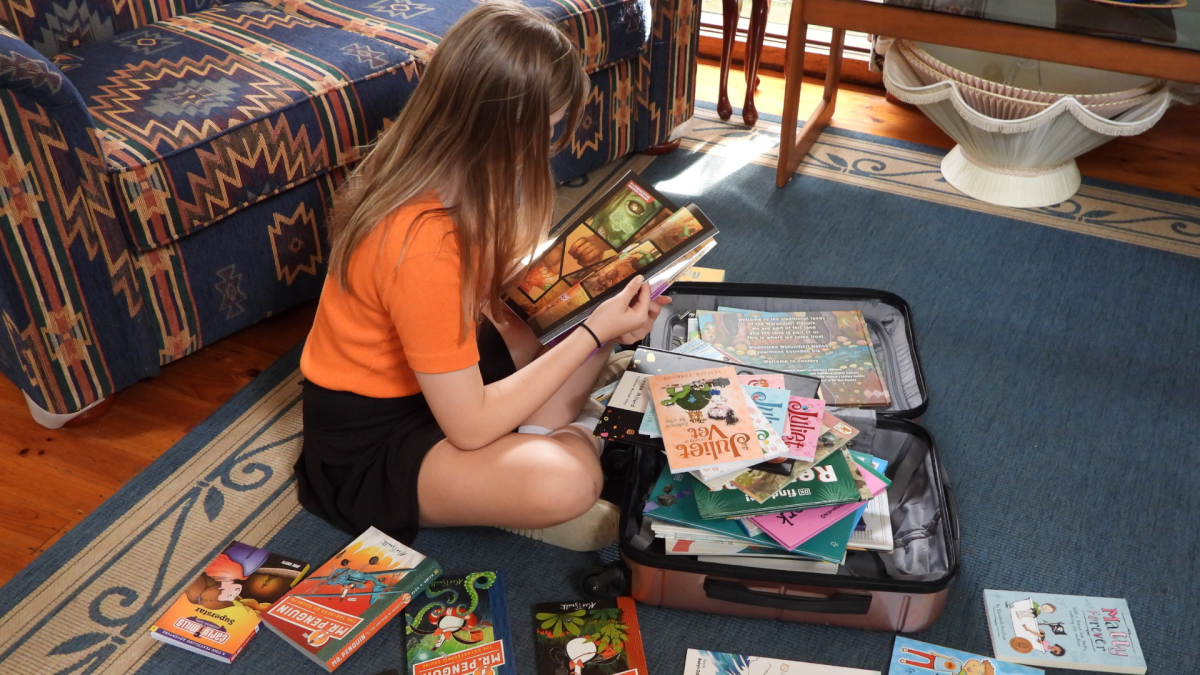 A girl sitting in front of a suitcase full of books.