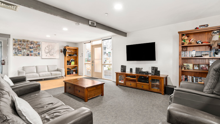 --Loungeroom with two couches and three arm chairs, a coffee table, TV unit and wall mounted TV.--