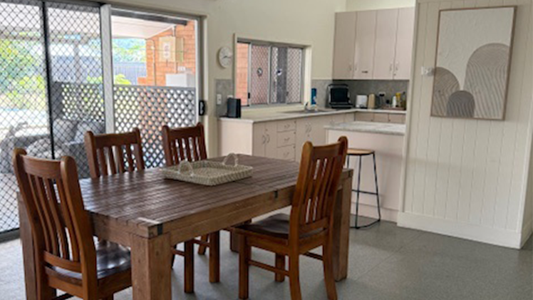 Light-filled open kitchen and dining space with wooden dining table, four chairs, and sliding doors leading to the outdoor area.