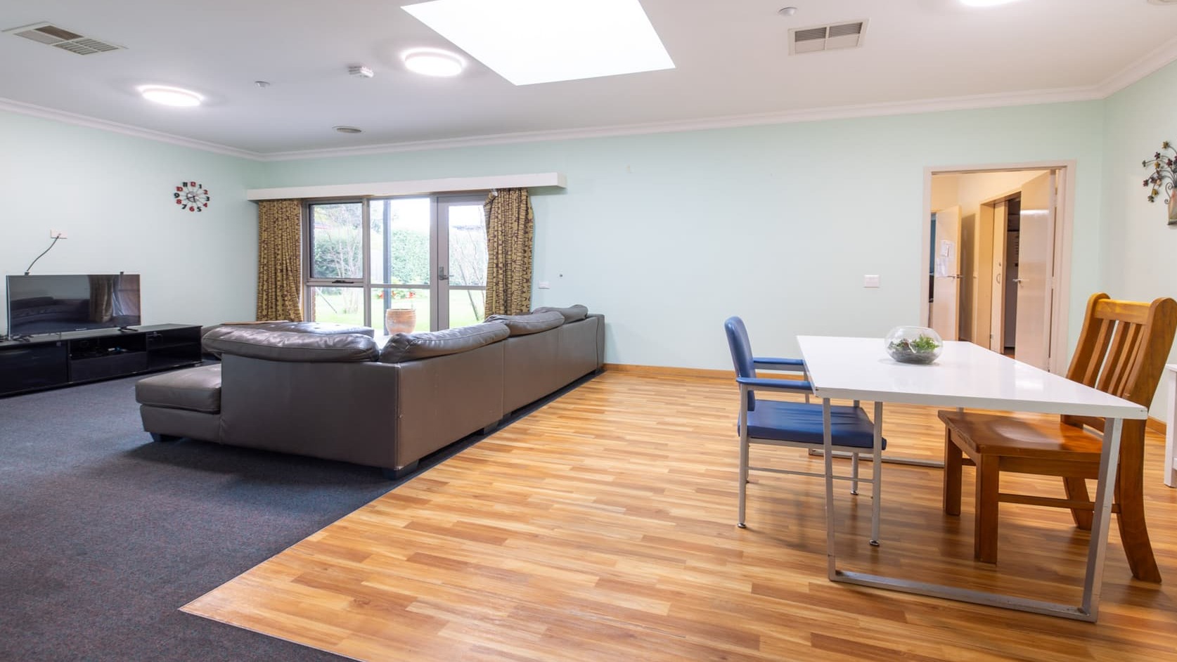Second living space with L shaped lounge facing a television and second dining table with two chairs on hard wood flooring.