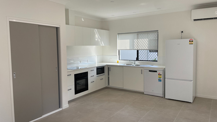 Large white tiled kitchen with a fridge, dishwasher, over, benchtop and split AC.