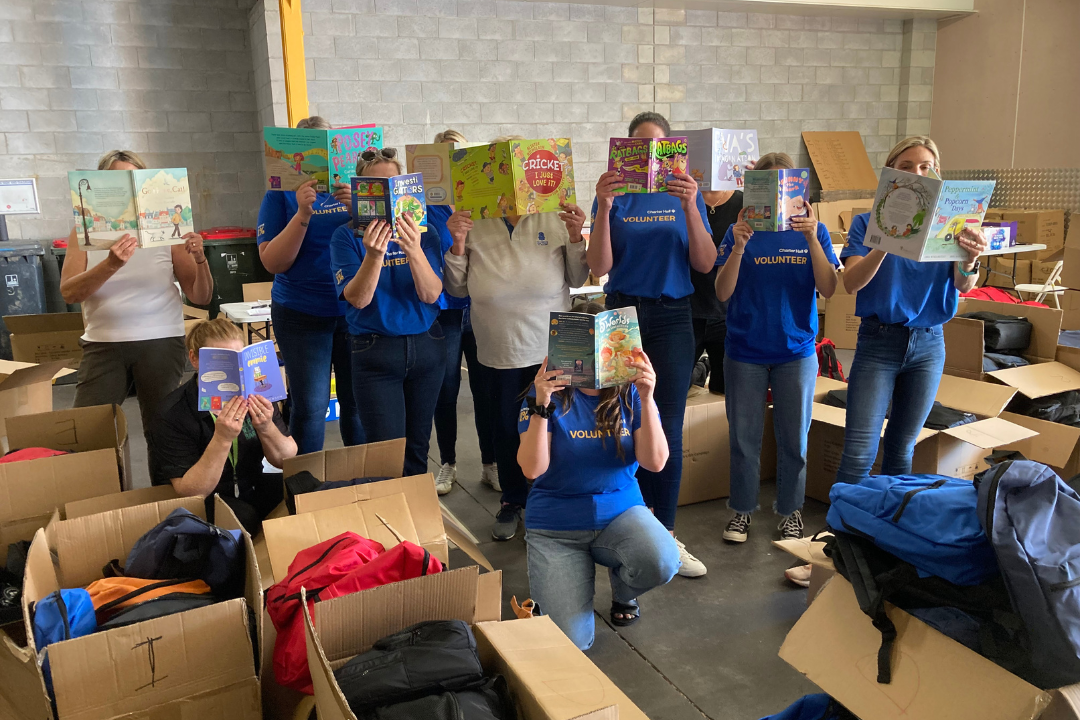 A group of staff and volunteers at the Book Backpack Packing Day, holding books over their faces.