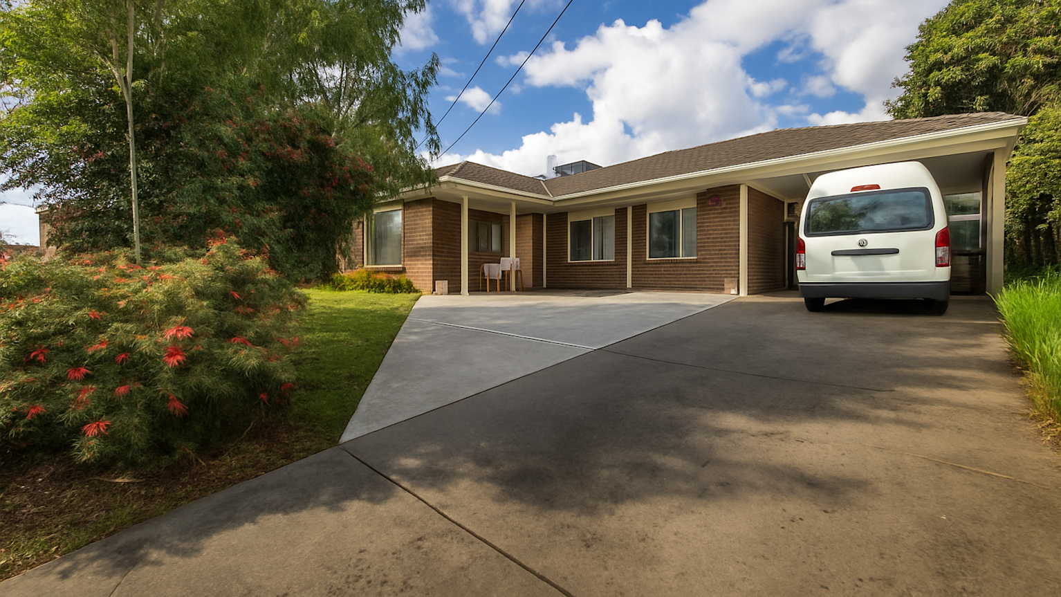 Single-storey brick home with driveway, garden with trees, and white van parked under carport.