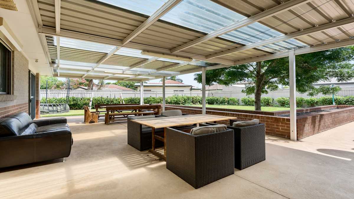 Undercover outdoor entertainment area with a picnic-style wooden table, a wooden table with four chairs and a black couch.