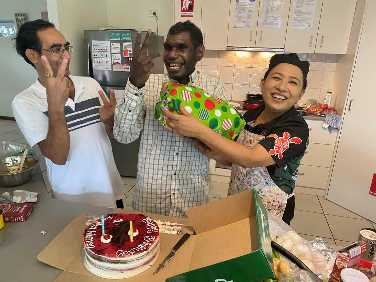 Three people standing behind a birthday cake smiling