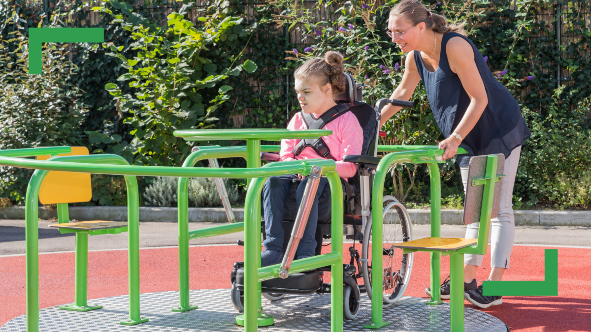 A girl in a wheelchair is at a playground with a person assisting her.