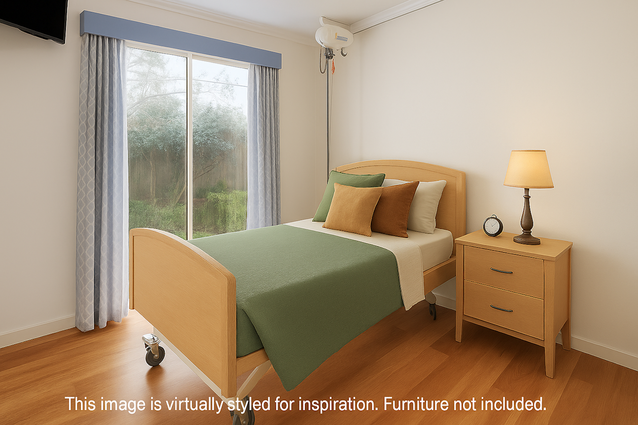 Bright bedroom with a hospital-style single bed featuring green and neutral-toned bedding, positioned beside a wooden nightstand with a lamp and clock. The room has light wooden floors, white walls, and a large sliding glass door with patterned curtains. A ceiling-mounted patient lift system is also visible. White text along the bottom reads: “This image is virtually styled for inspiration. Furniture not included.”