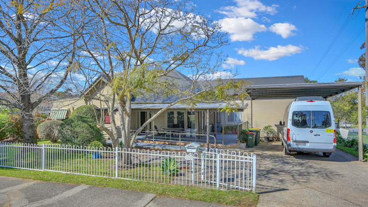 Single-storey house with front veranda, garden, and driveway with carport and parked van.