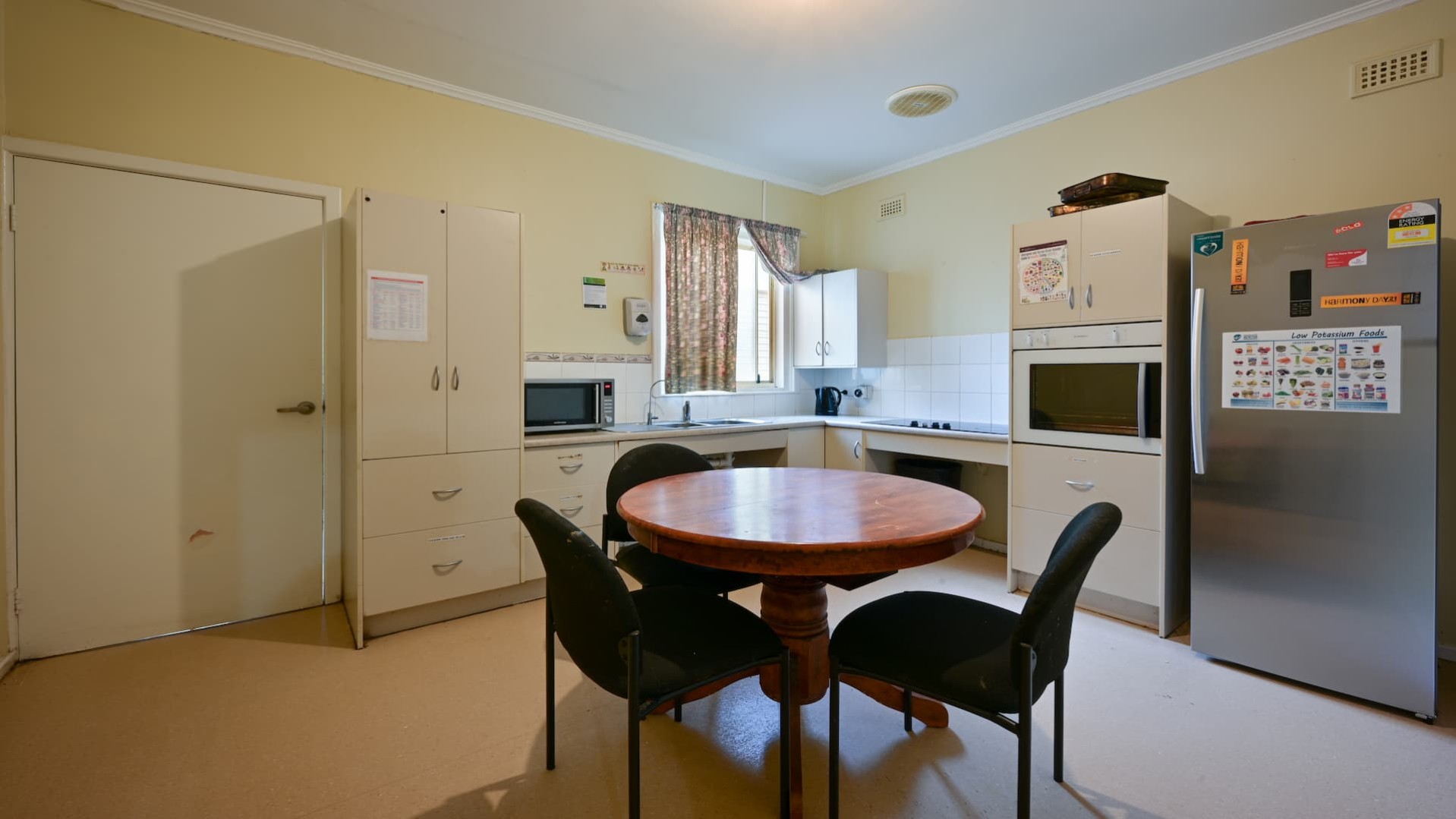 --Kitchen with cream cabinets and benches, a microwave, oven, stove, fridge and round dining table.--