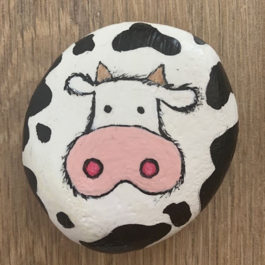 A rock handpainted to look like a black and white cow.