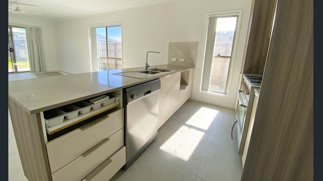 Modern kitchen with island bench, double sink, stainless steel appliances, and ample natural light."