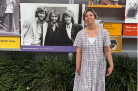 Nicolette enjoying her holiday in Redcliffe, she is wearing a long pale dress and standing in front of posters.