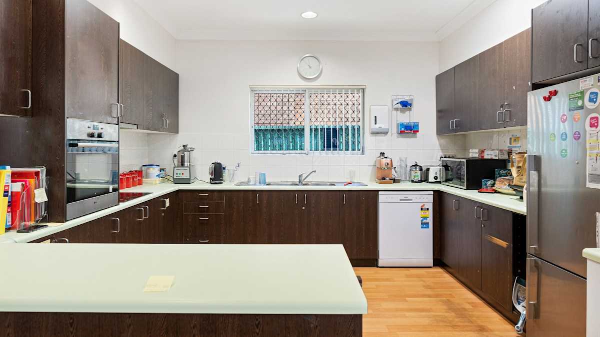 Modern kitchen with brown cupboards and cream bench tops.  Includes large fridge, dishwasher, oven and stove top, microwave.