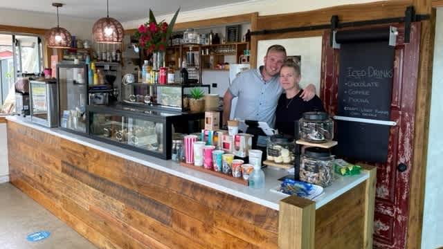 Lleyton is standinng behind a cafe bar with his arm account a woman.