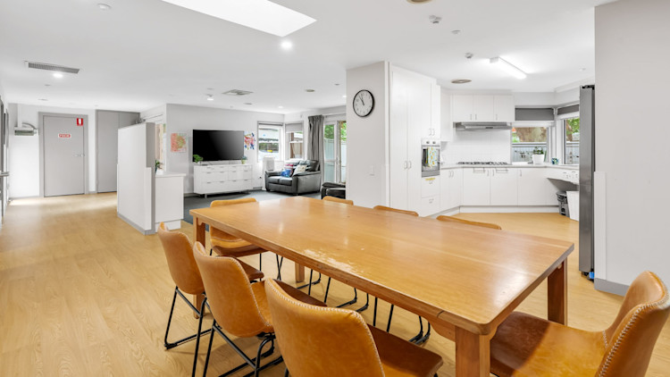 Wide view of the open kitchen and dining space with timber flooring and white cupboards.