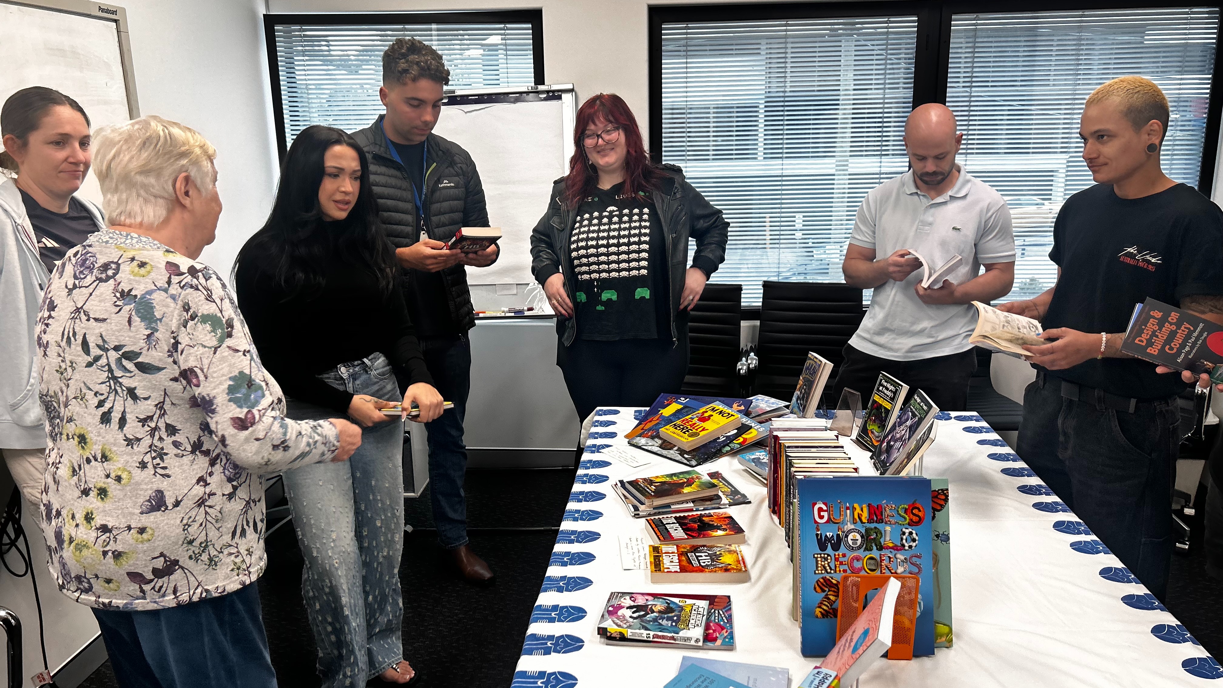 Staff gathered around a table with books on display on top of a table cloth with the the Children’s Book Council of Australia logo.